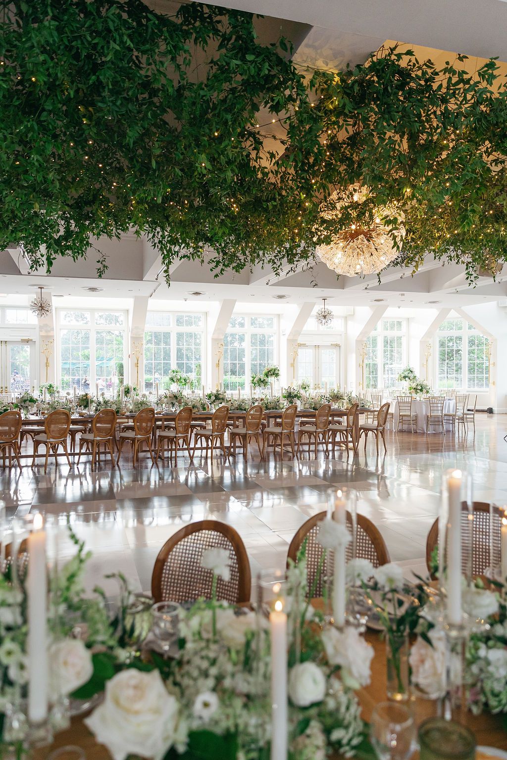 Elegant wedding reception venue with hanging greenery and white floral centerpieces on round tables.