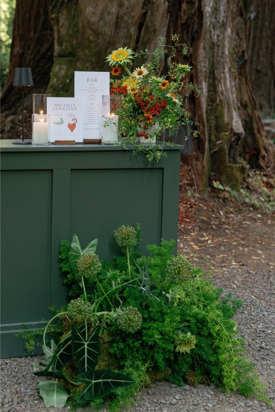 Rustic outdoor green cabinet decorated with orange and yellow wildflowers against a wooded backdrop.