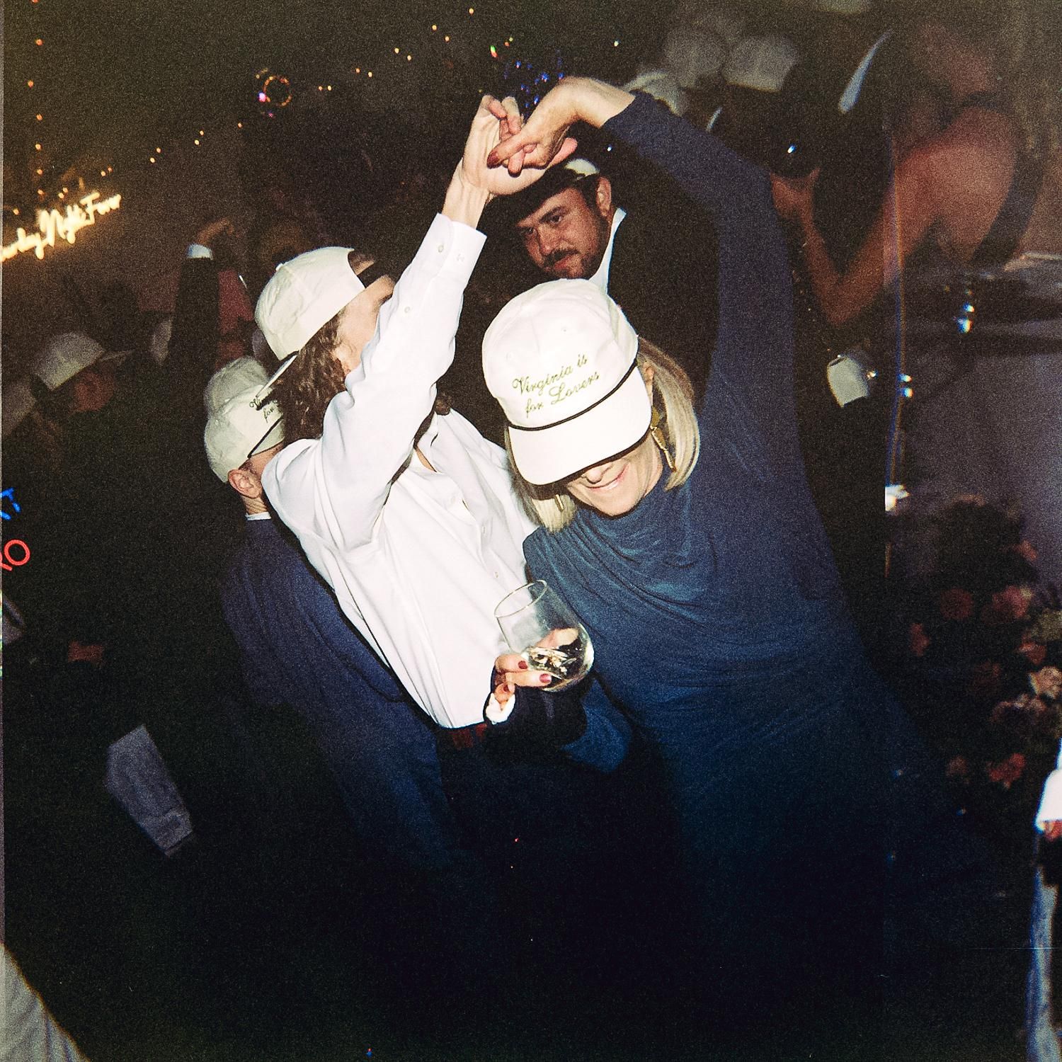 Pair dancing at a western dance event with the dancer in white hat performing a dip move in a backlit setting.