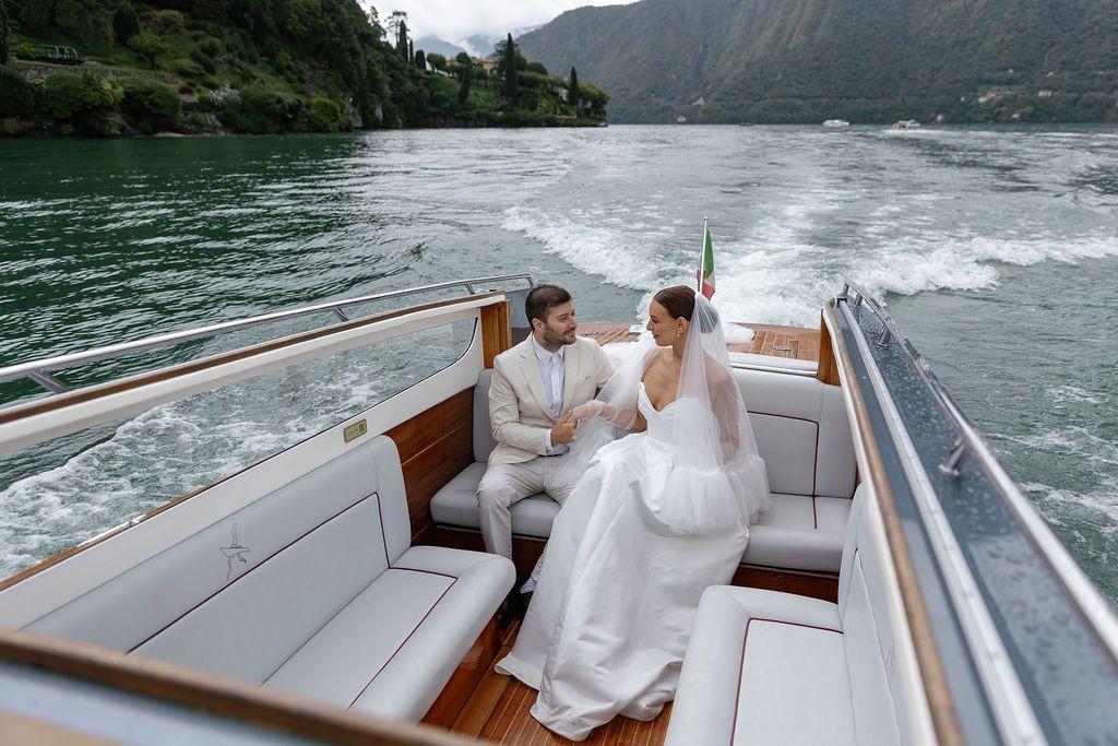 Newlyweds enjoy a boat ride across a scenic mountain lake with white wake trailing behind in Lake Como.