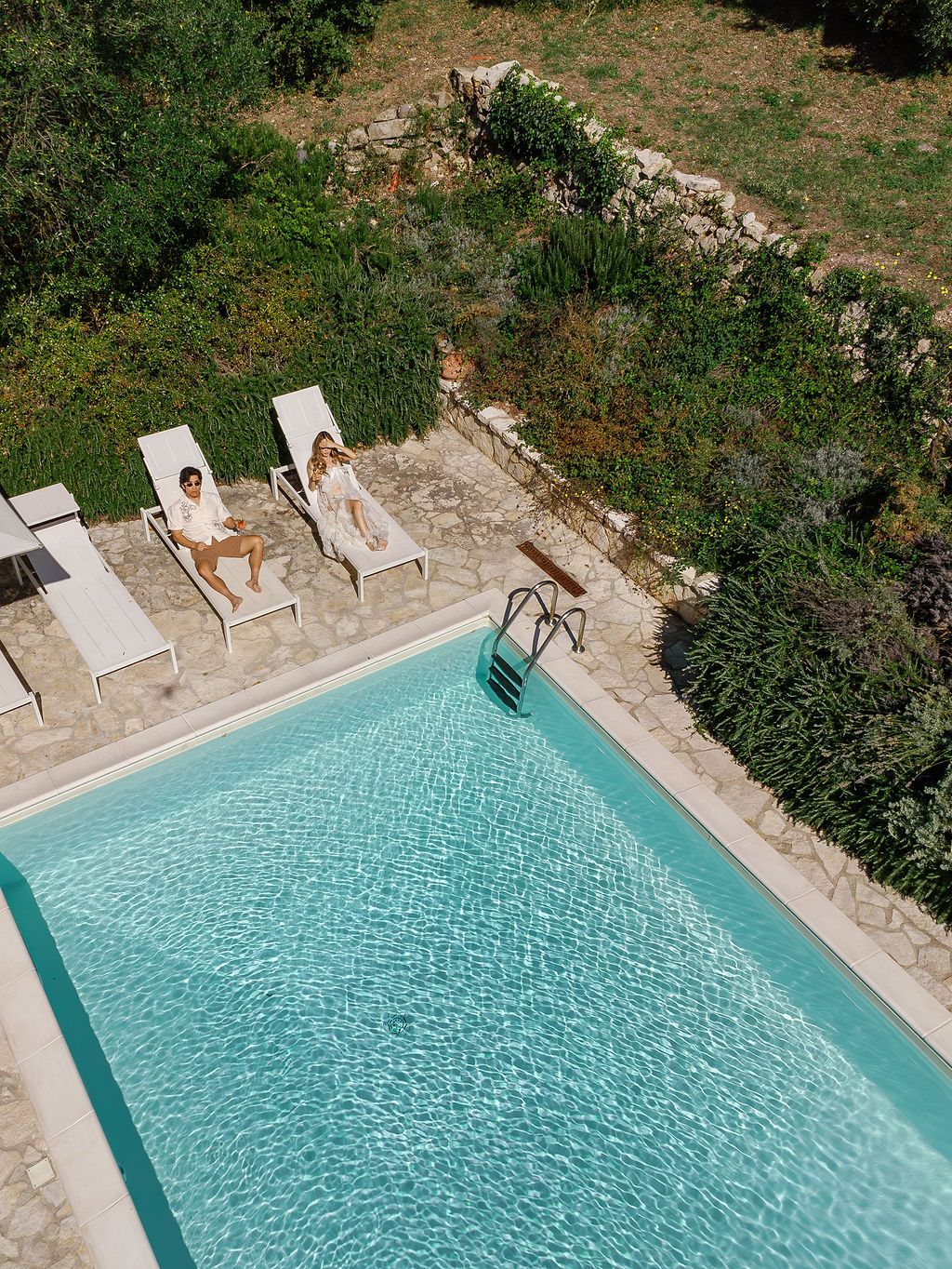 A sequence of five aerial shots showing a turquoise swimming pool surrounded by loungers and greenery in Tuscany, Italy.
