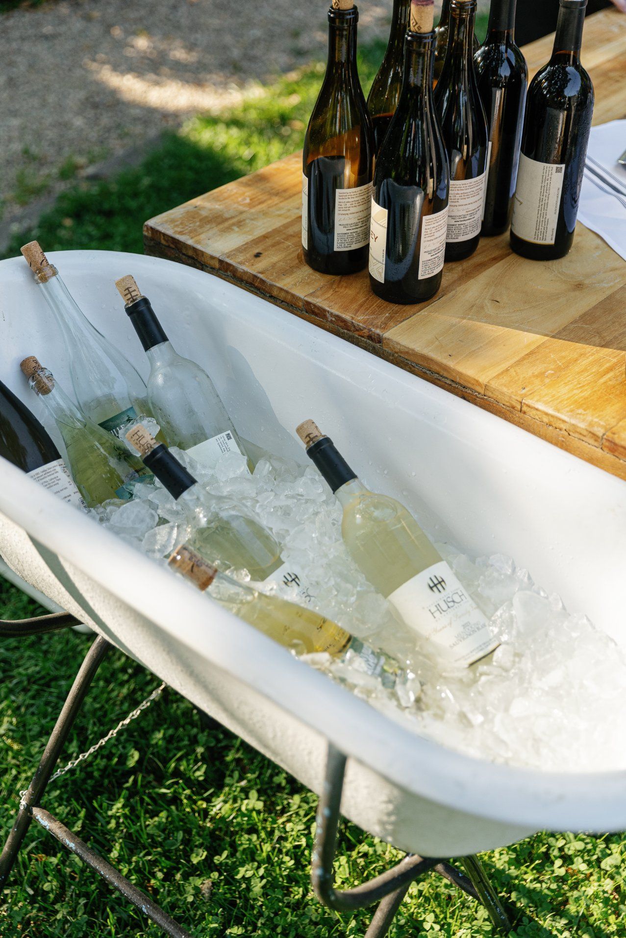 Wine bottles chilling in a white bathtub filled with ice at an outdoor event.