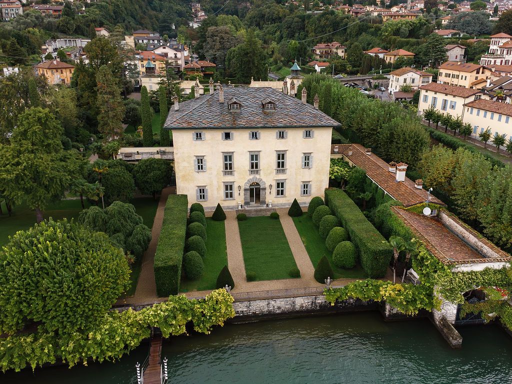 Aerial view of elegant Italian villa with manicured gardens on Lake Como waterfront.