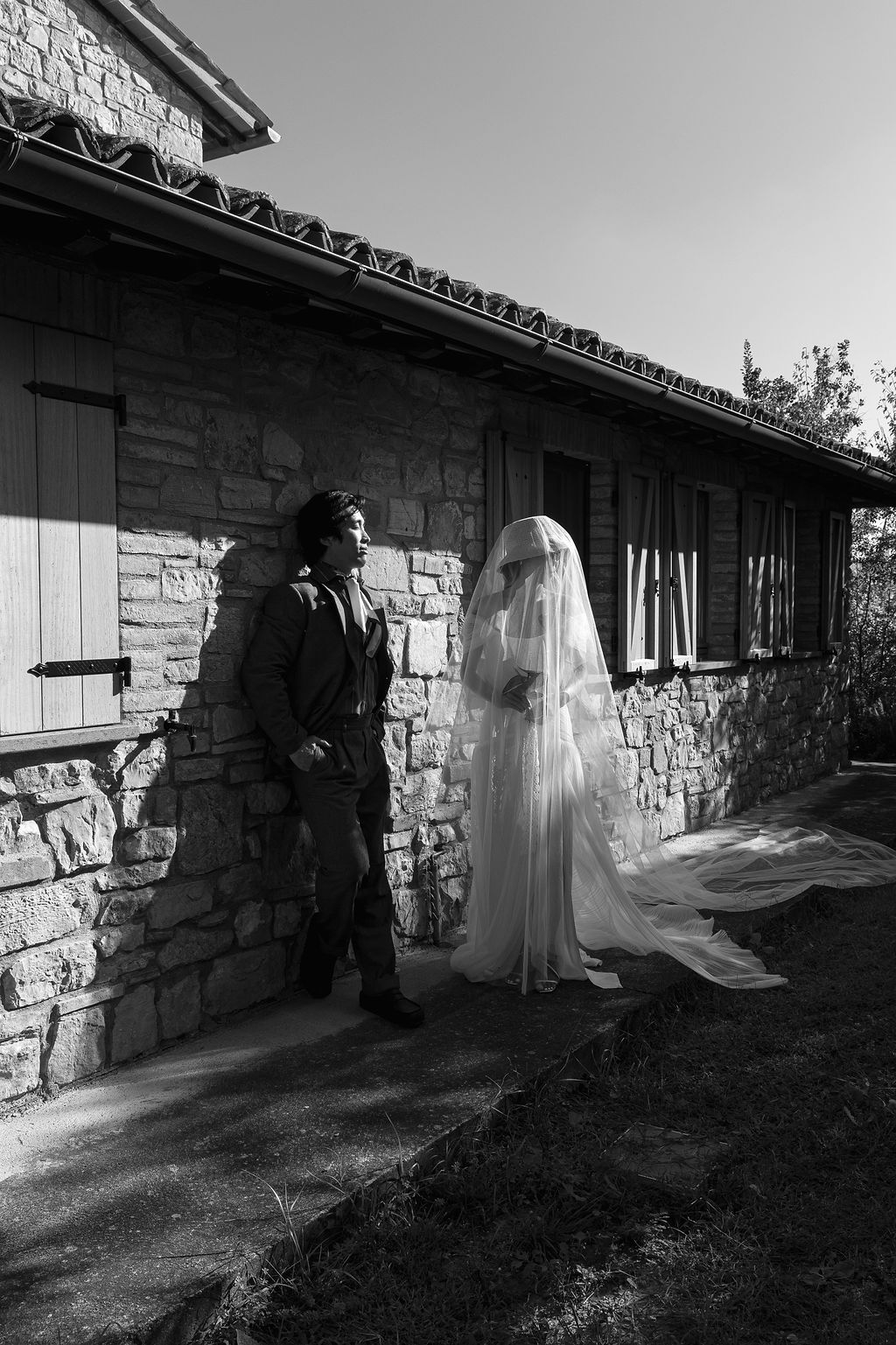 Black and white wedding photos of a couple standing against a rustic stone wall in dramatic lighting in Tuscany, Italy.