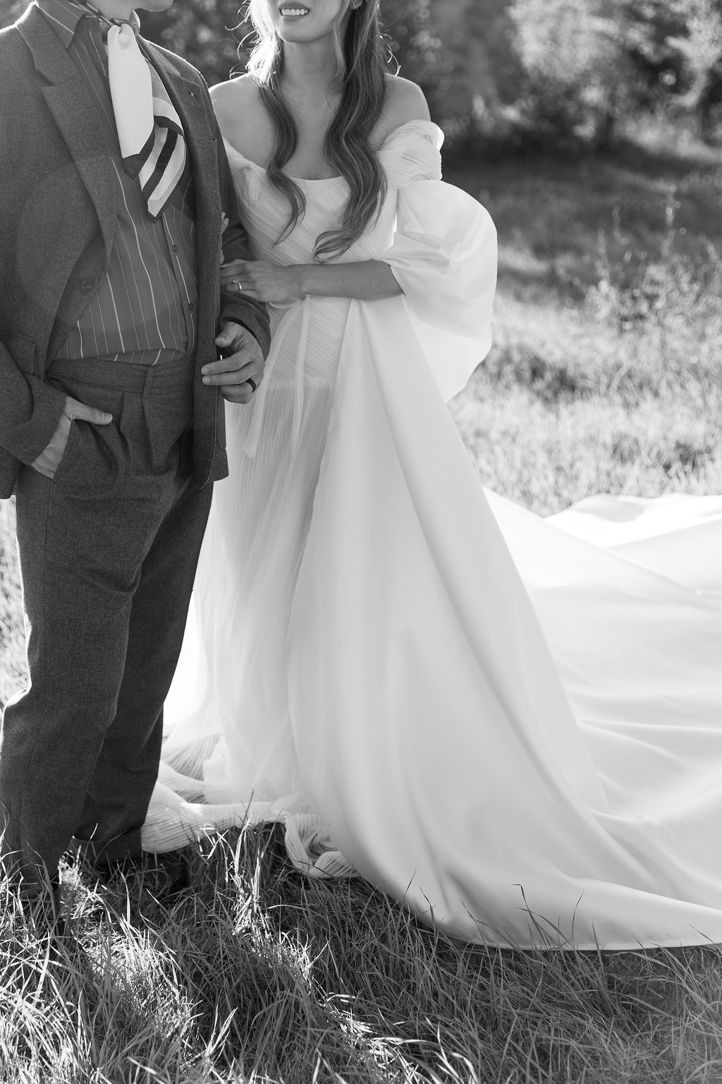 Elegant white wedding dress flows across grassy field during an outdoor photoshoot in Tuscany, Italy.