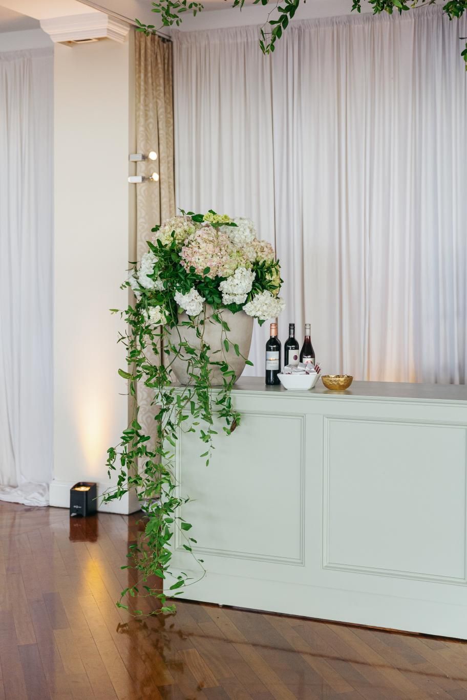 Elegant wedding venue interior with mint green wainscoting, flowing white curtains, and climbing ivy decorations.