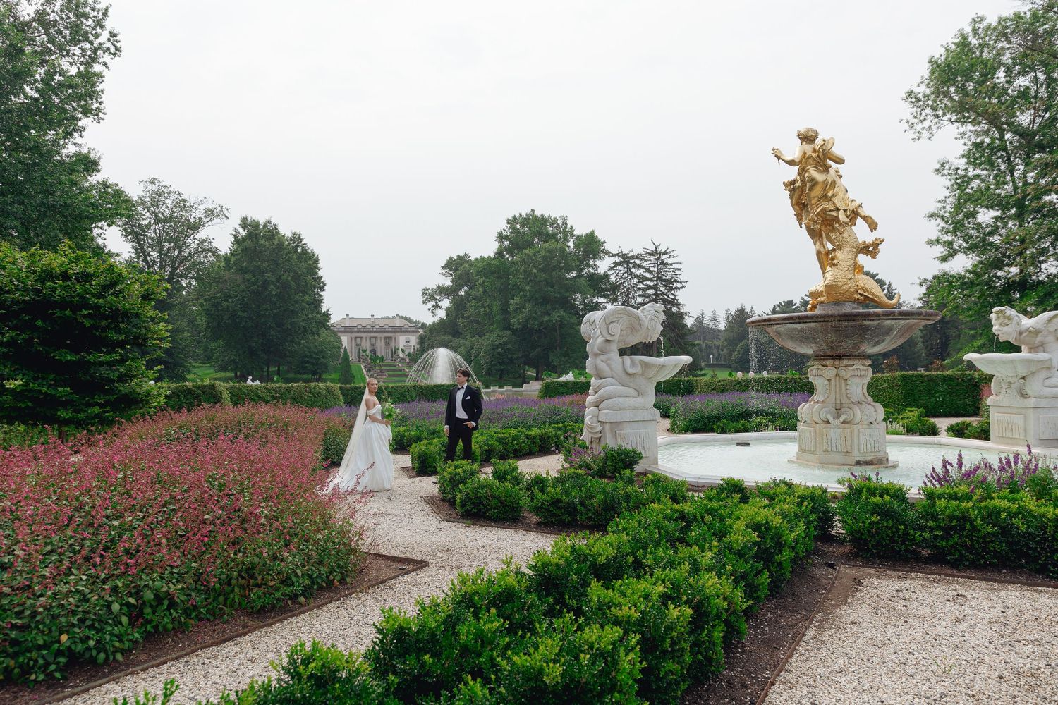 A scenic garden pathway features ornate stone sculptures and blooming flowers along a winding gravel walkway in France.
