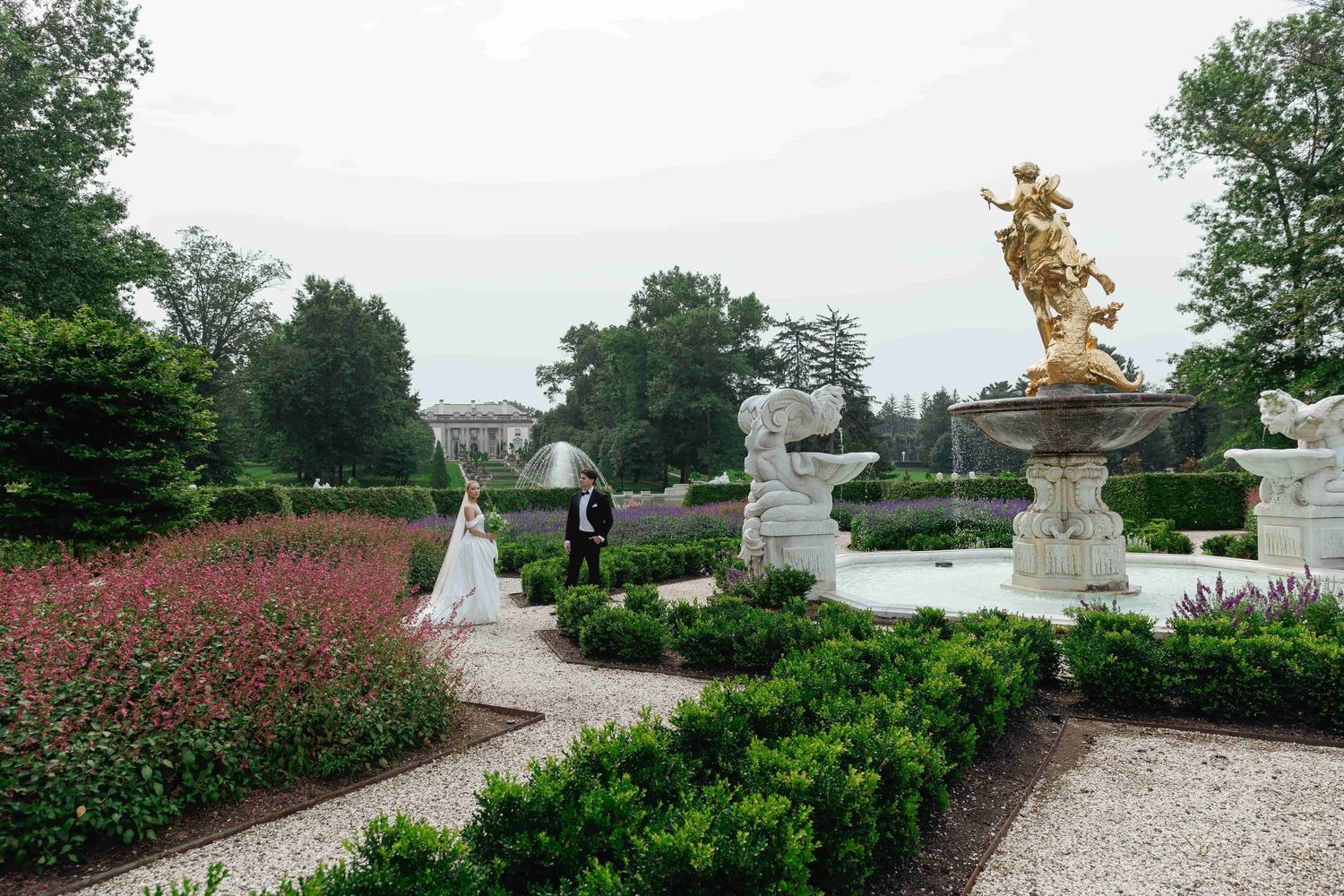 Formal garden path with pink flowers and ornate golden statues at the Nemours Estate in Delaware.