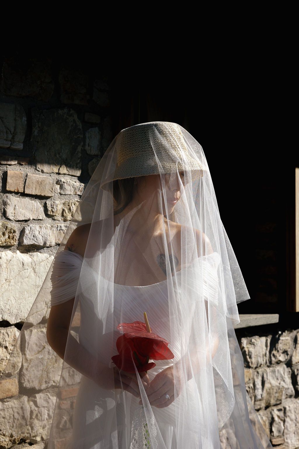 A delicate white veil with red floral accents drapes against a stone wall background.