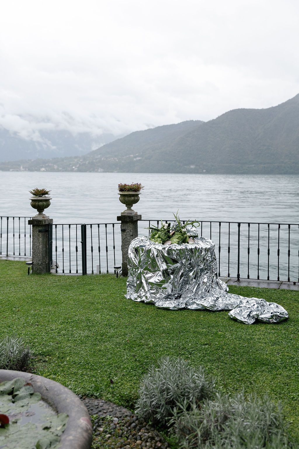 Decorative silver metallic sculptures arranged along a lakeside railing with misty mountains in the background in Lake Como.