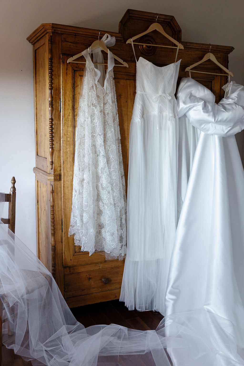 Multiple white wedding dresses hanging in a wooden wardrobe with elegant lace details in Tuscany, Italy.