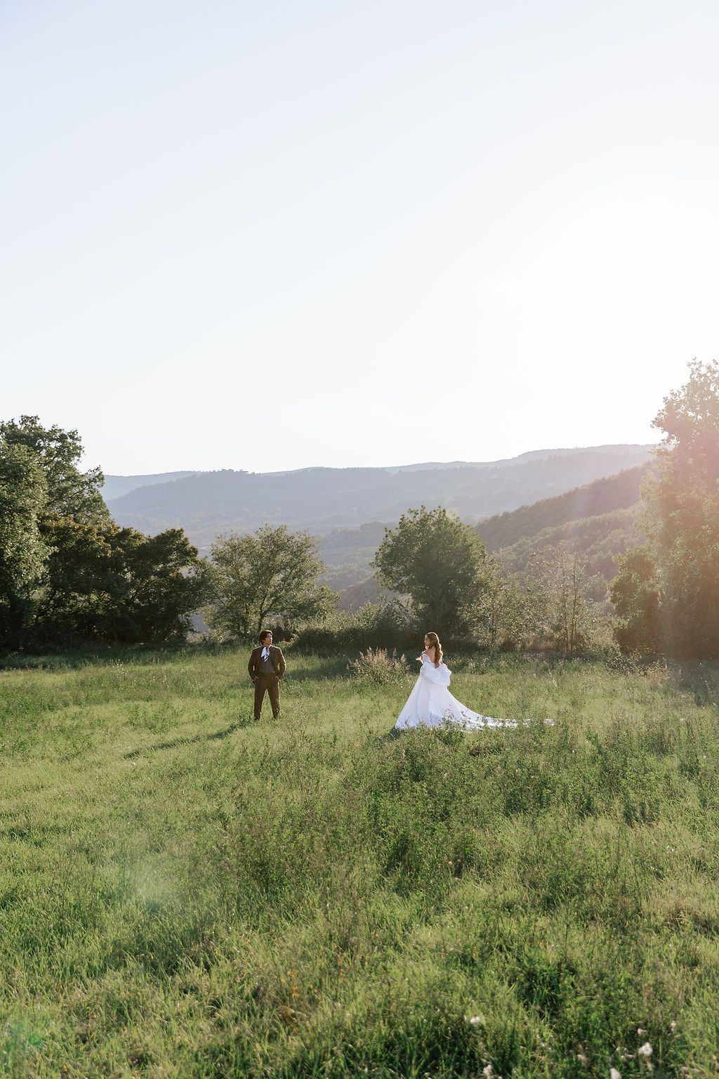 Two figures in a grassy mountain meadow during a wedding photoshoot at sunset in Tuscany, Italy.