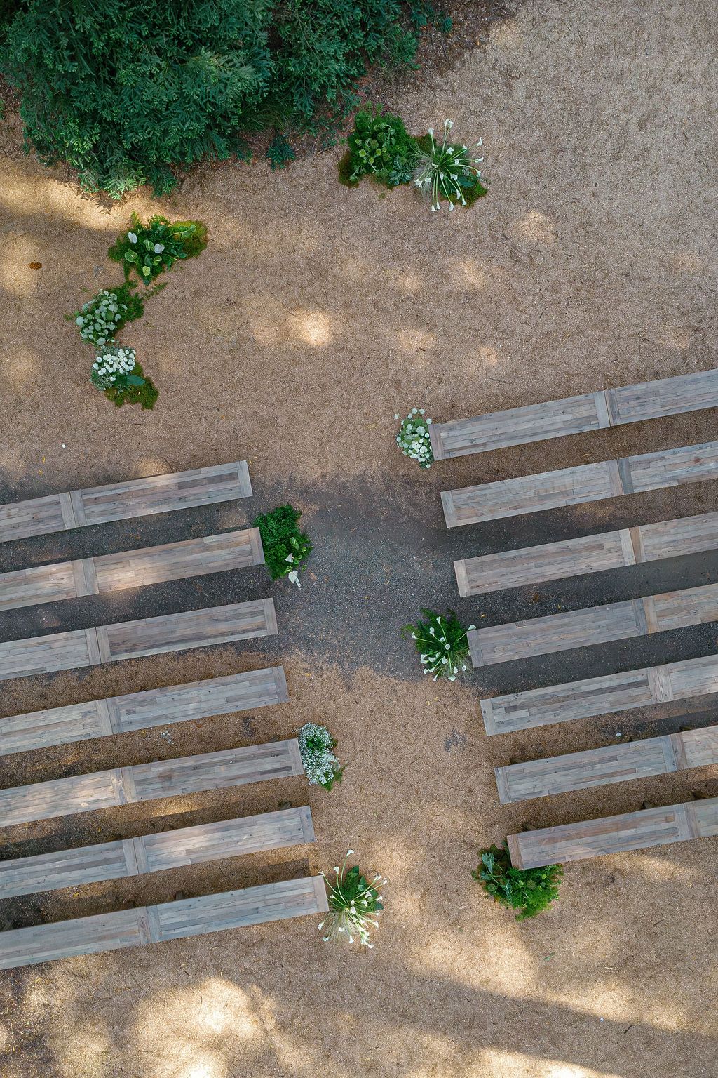 Wooden benches arranged in rows on a dirt ground create an outdoor seating area surrounded by greenery.
