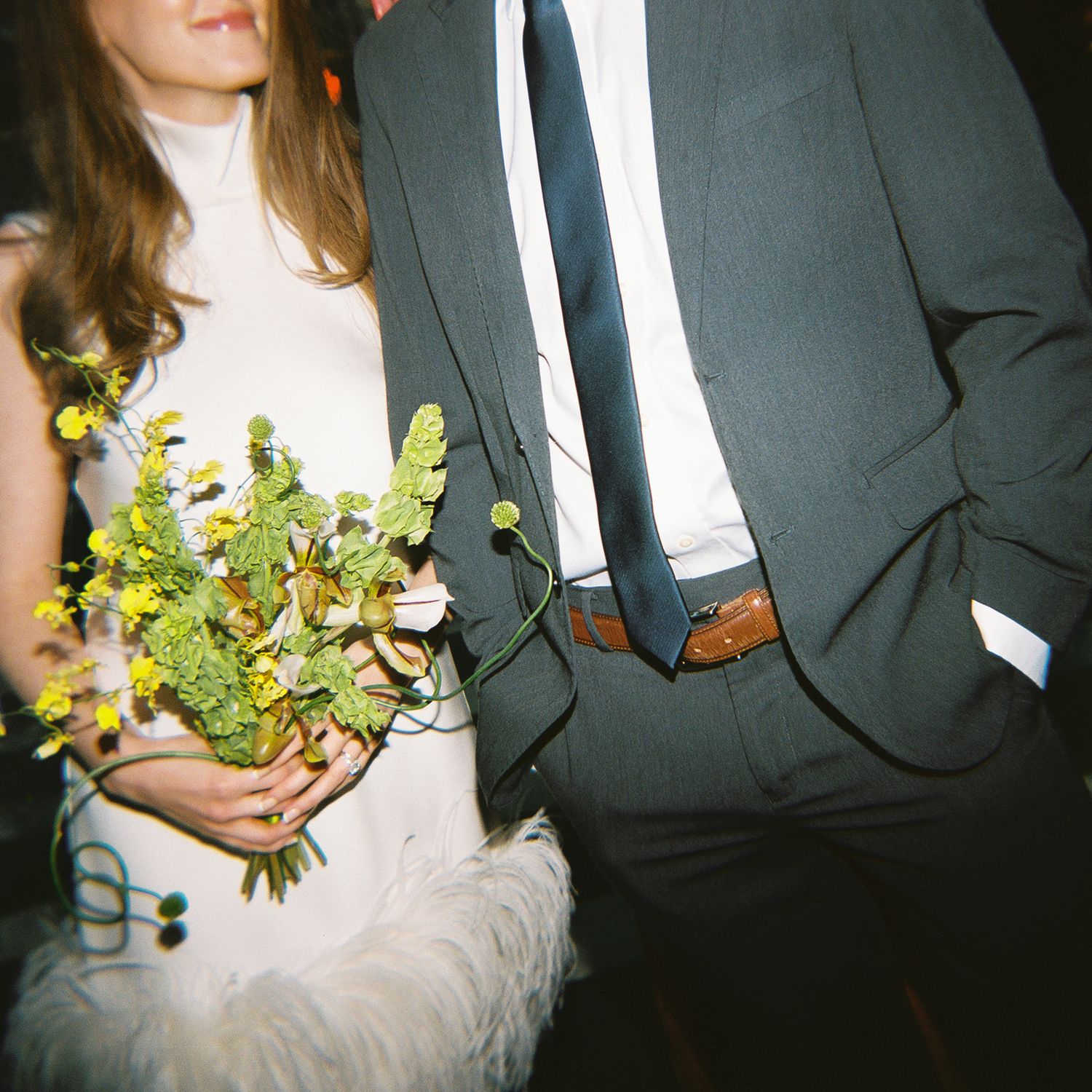 Bride holding yellow wildflower bouquet beside groom in gray suit at wedding reception.