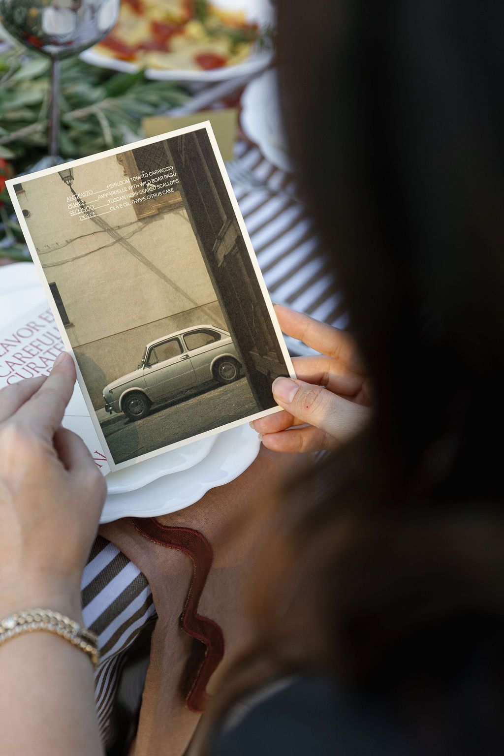 Someone holds a vintage photograph showing a classic car parked on a street in sepia tones in Tuscany, Italy.
