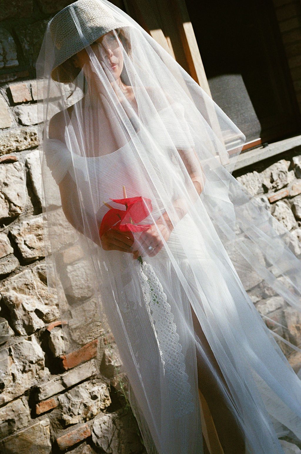 Artistic bridal portraits with flowing veil against stone wall texture in natural light in Tuscany, Italy.