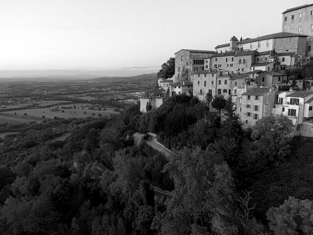 Black and white aerial view of a historic hilltop town in Tuscany with stone buildings perched along steep cliffs.