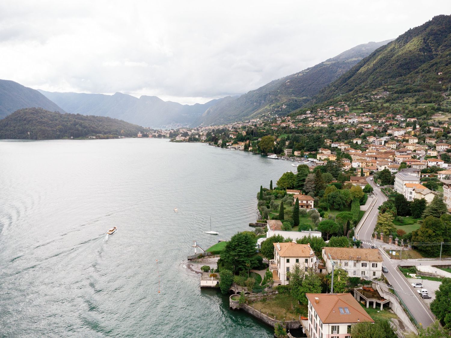 Aerial view of a picturesque Italian lakeside village on Lake Como, surrounded by mountains and lush greenery.