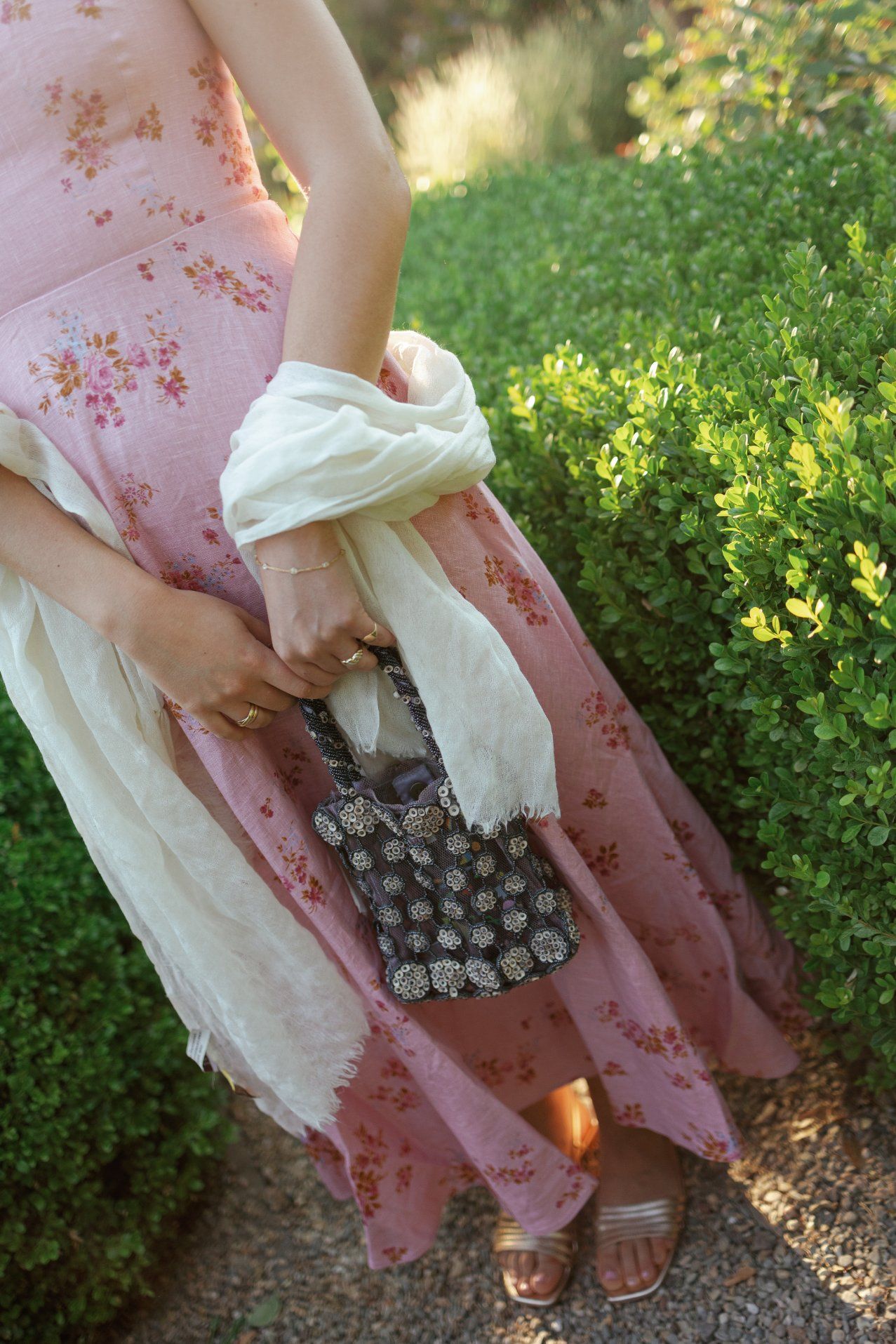 A person wearing a pink floral dress holds a vintage ice cube tray in a sunlit garden setting.