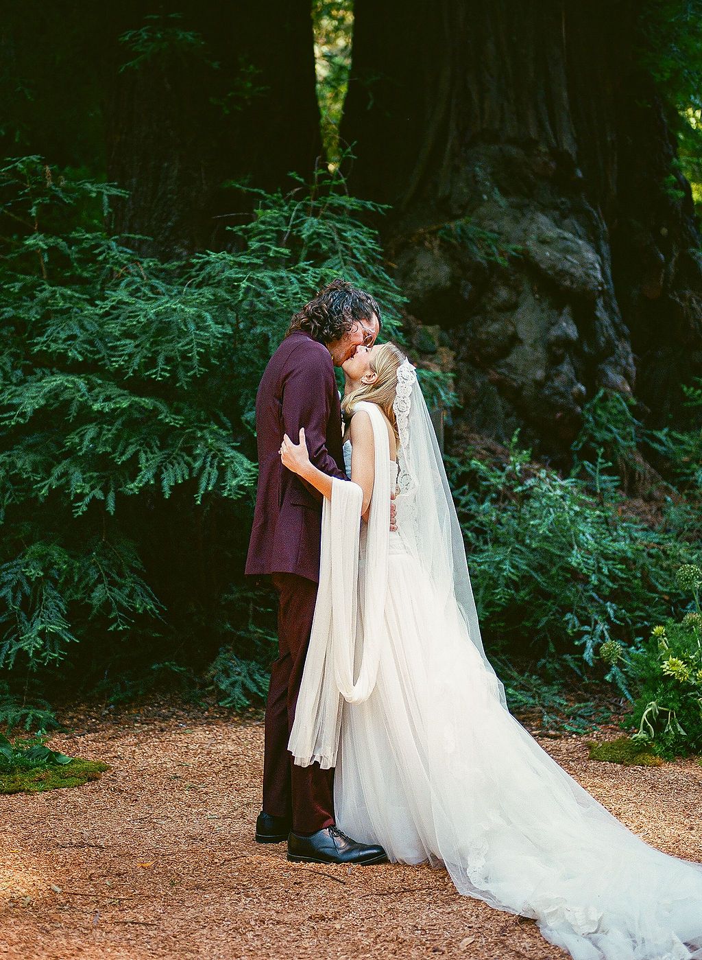 Wedding couple sharing an intimate moment on a forest path surrounded by lush greenery.