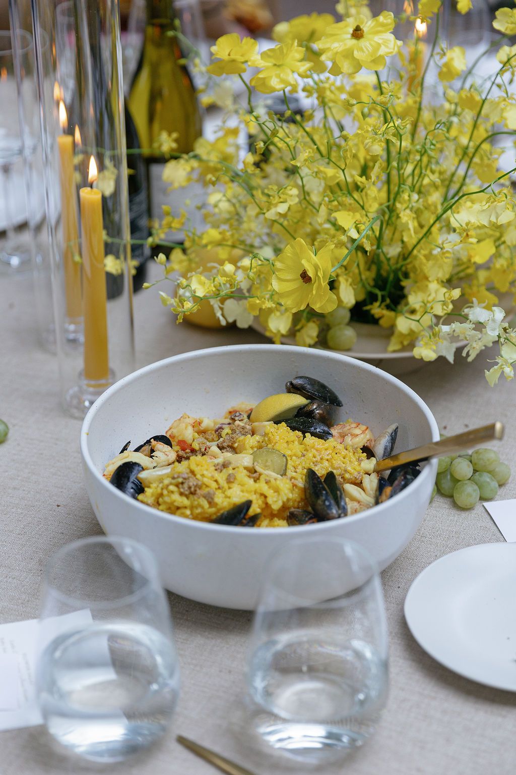 Yellow flowers decorate a table setting with white bowls and glassware.