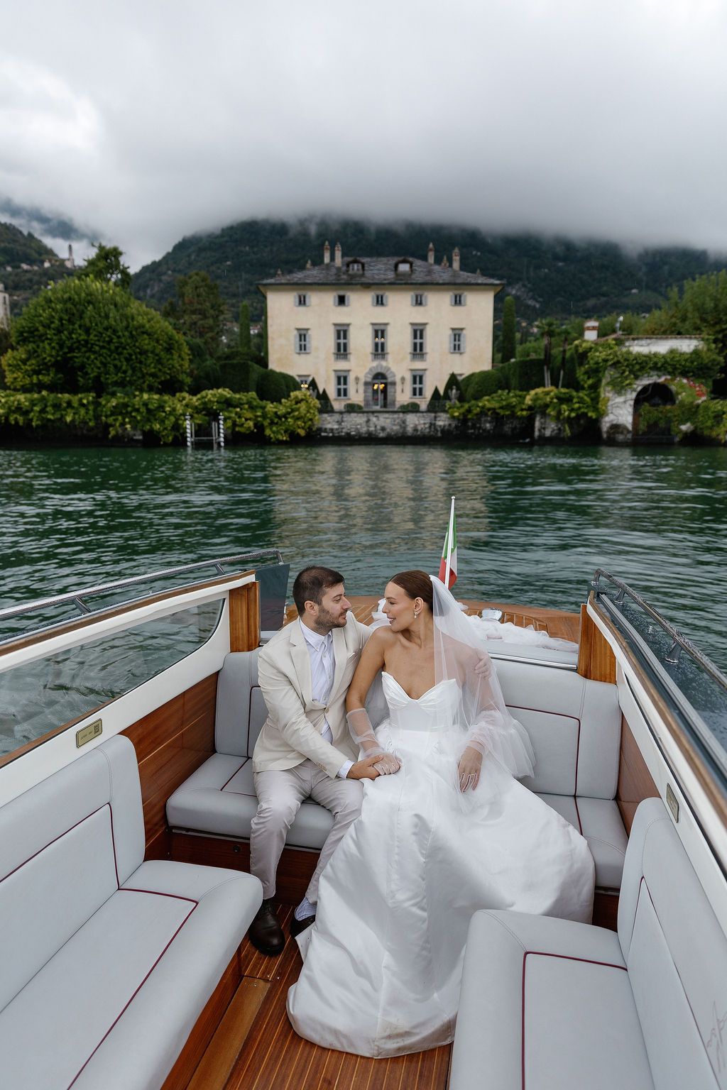 Couple enjoying a romantic boat ride on Lake Como with misty mountains and Italian villas in the background.