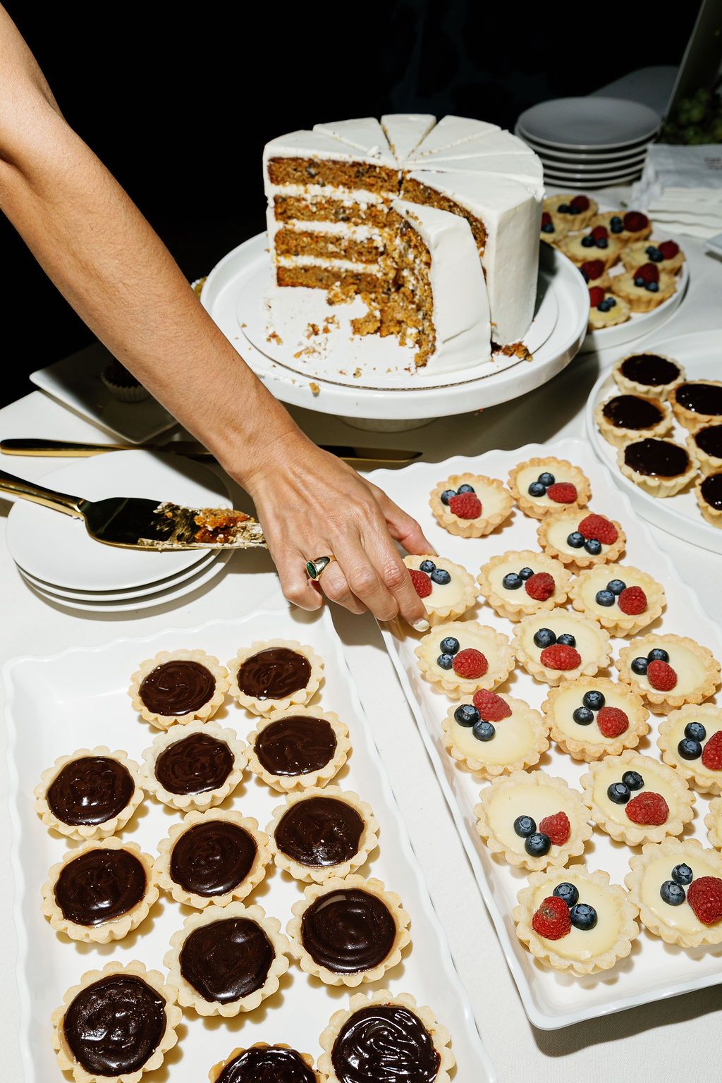 Dessert table with a layered white cake and assorted tarts featuring chocolate and fresh berries on display.