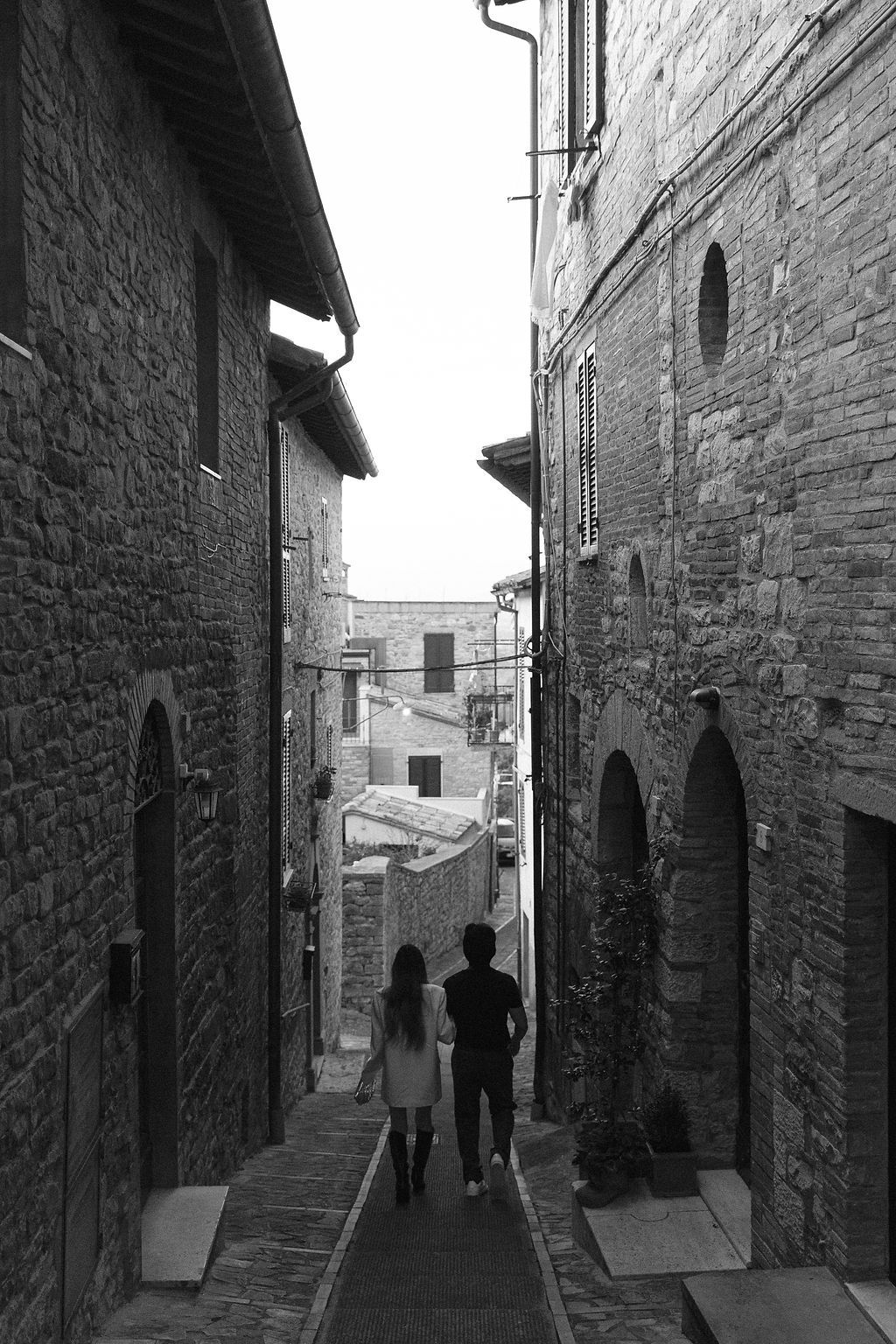 Silhouettes of people walking through narrow medieval stone alleyways in a historic Italian village in Tuscany, Italy.