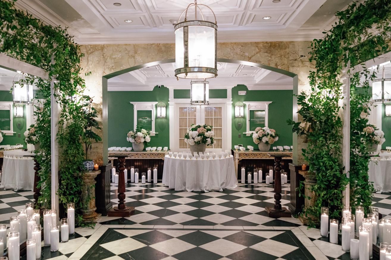 Panoramic view of an elegant ballroom interior with black and white checkered floors and lush greenery decorations.