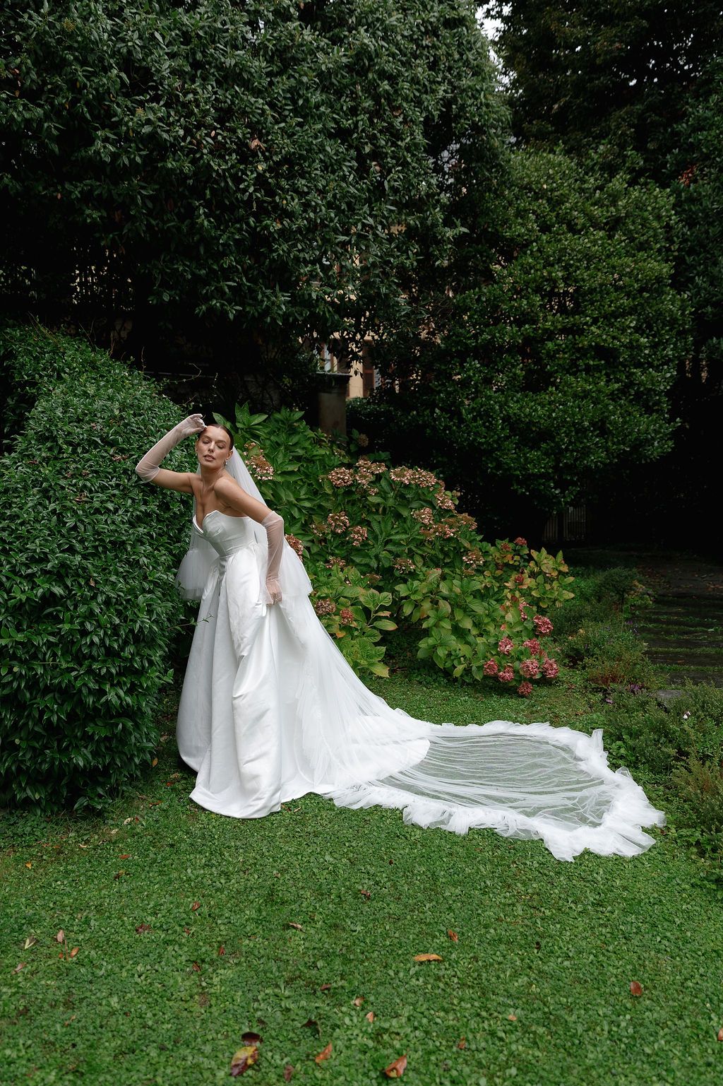 Flowing white wedding gown with long train displayed in a lush garden setting in Lake Como.