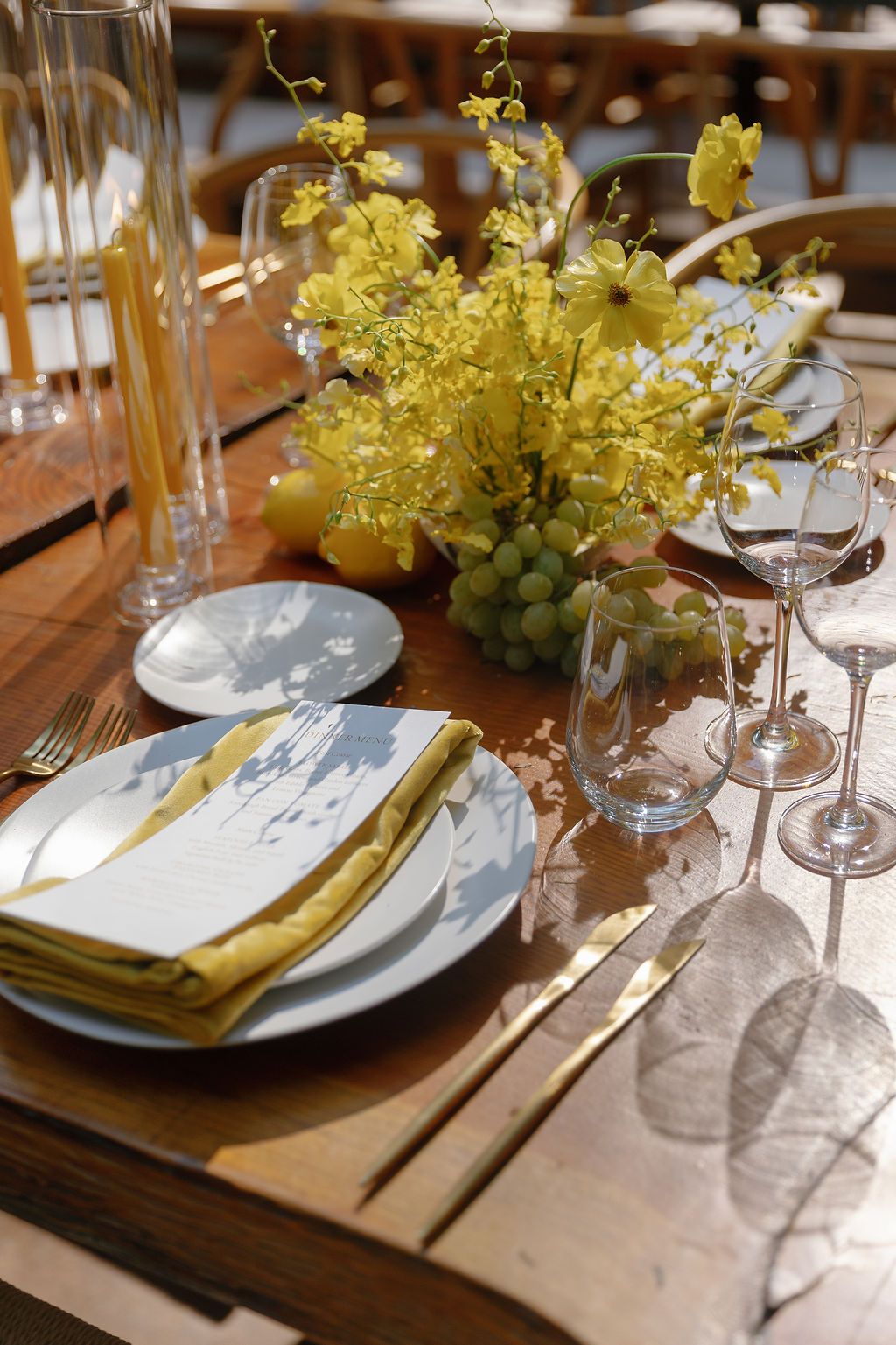 Elegant table setting with yellow floral centerpieces, wine glasses, and place settings on wooden table.