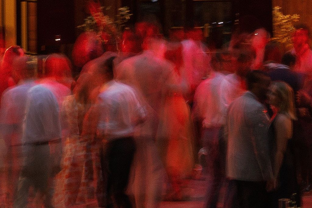 A crowd of people dancing at a dimly lit party venue with red lighting creating an atmospheric glow.