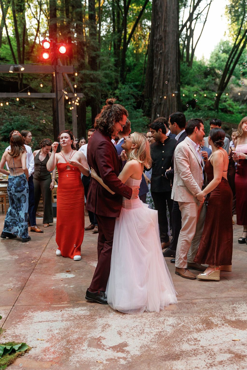 Wedding reception dance floor under string lights in a wooded outdoor venue.