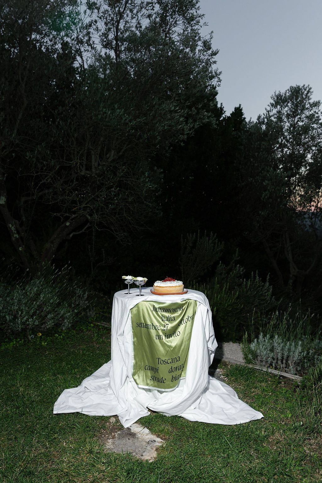 White and green fabric draped over tables in a twilight garden setting creates an ethereal outdoor scene.