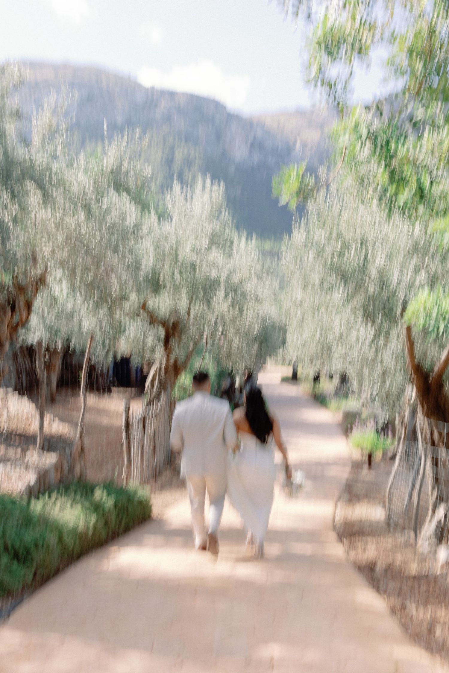 Couple walks hand-in-hand down a tree-lined path with mountain views on their wedding day.
