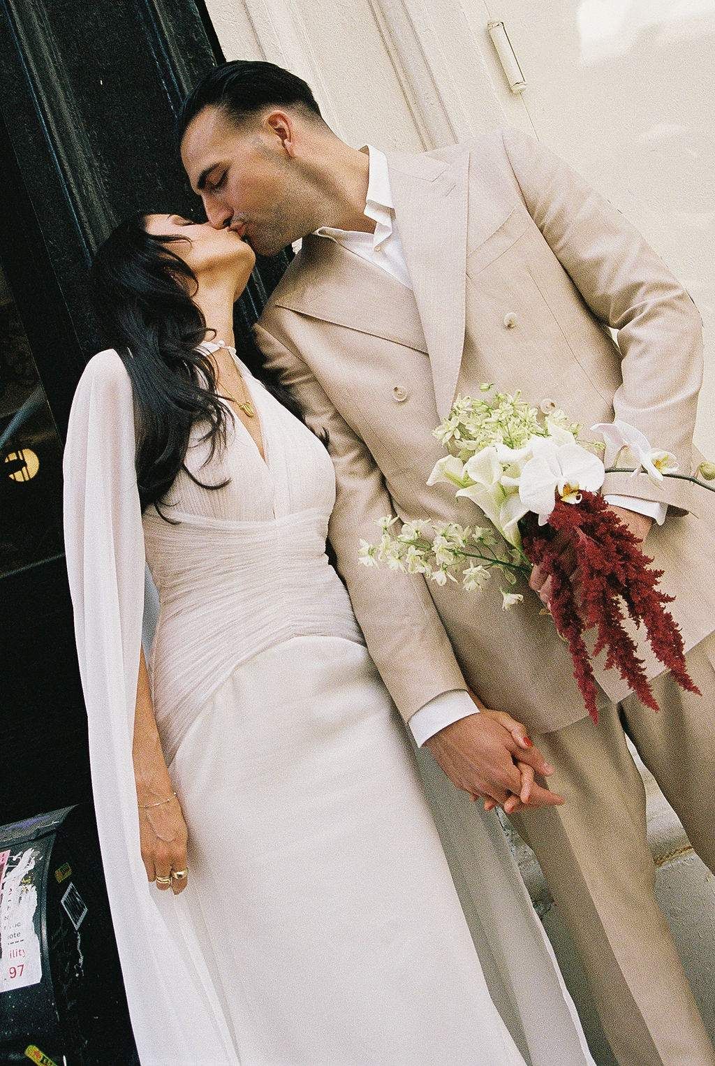 A romantic wedding moment captured with a couple in white and beige embracing while holding a bouquet with burgundy accents.