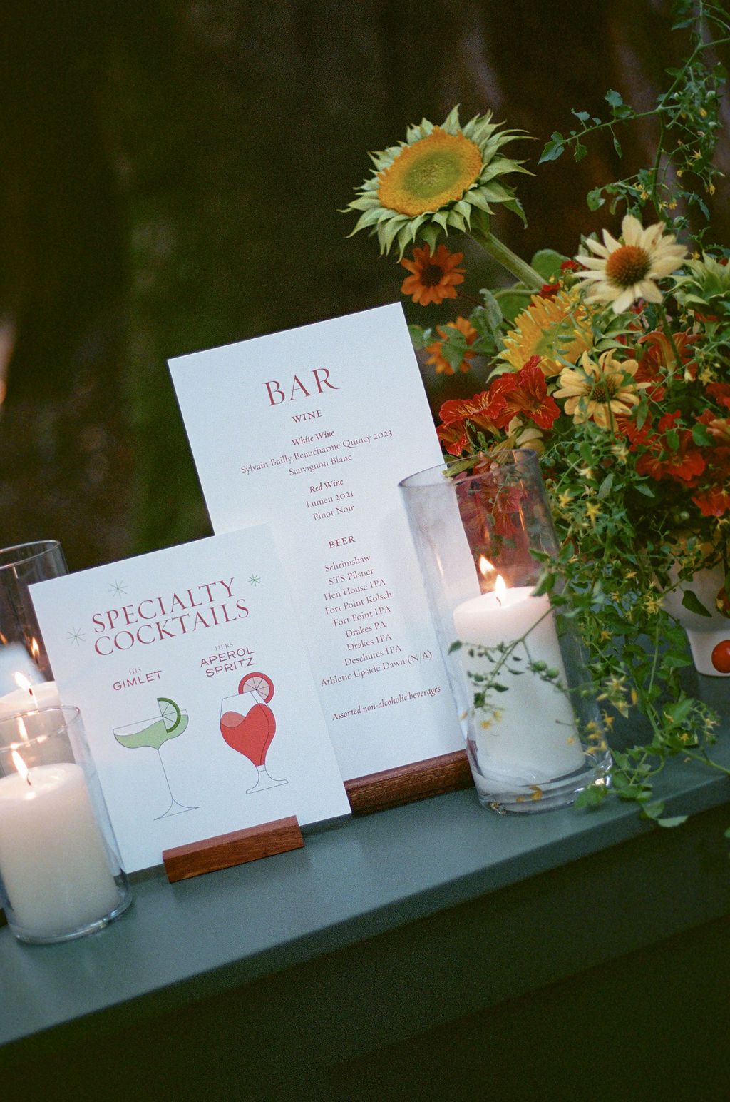 Bar menu signs and lit candles displayed with sunflowers at an outdoor wedding reception.
