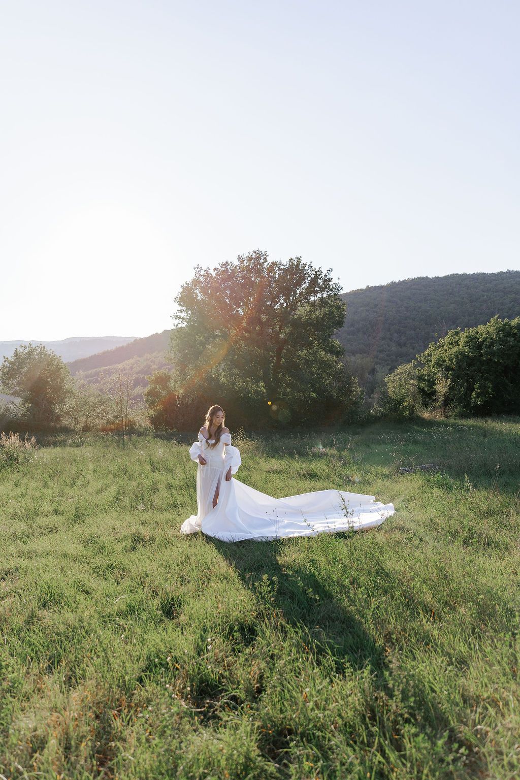 A flowing white wedding dress catches sunlight in a scenic mountain meadow during golden hour in Tuscany, Italy.