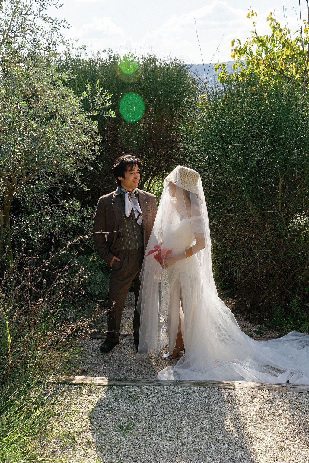 A romantic wedding photoshoot sequence showing a couple posing together on a garden path surrounded by greenery in Tuscany, Italy.