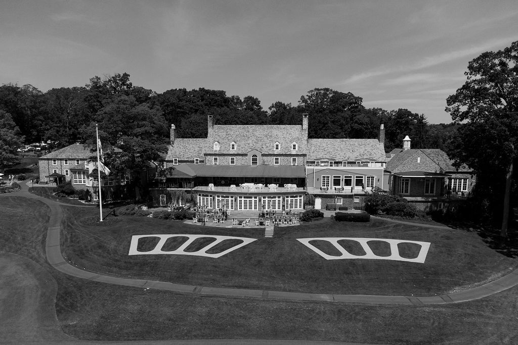 A black and white aerial view of a large colonial style mansion with landscaped terraces and driveways.