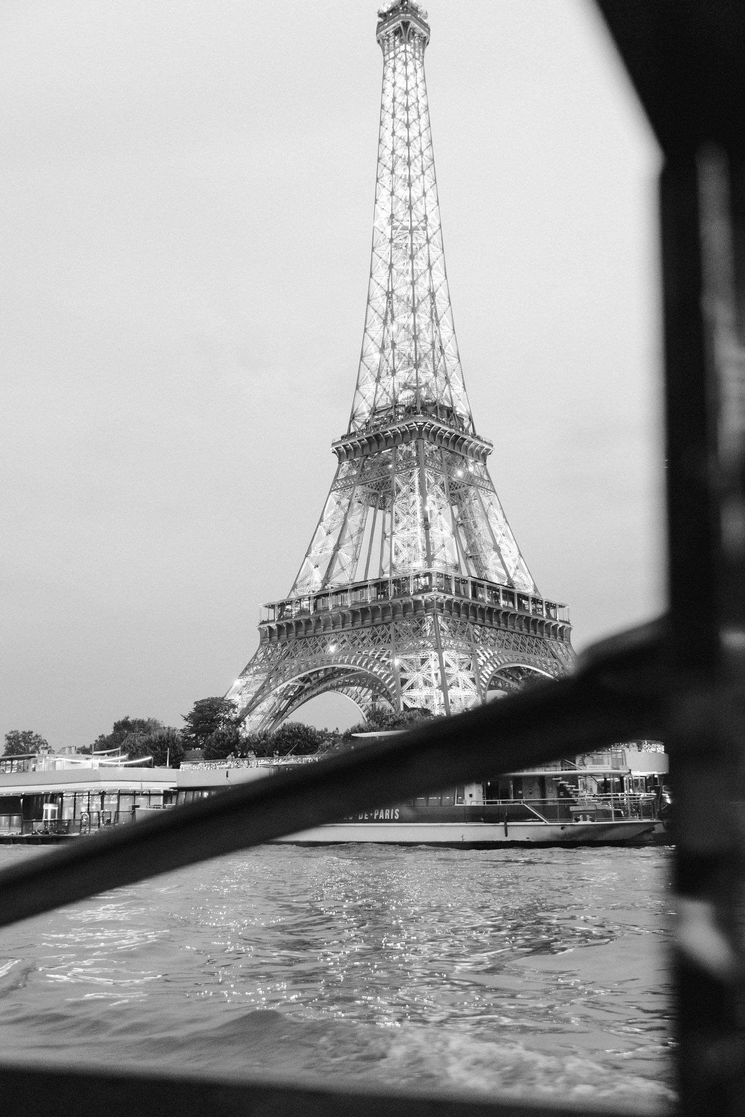 Black and white photo of the illuminated Eiffel Tower viewed from the Seine River in Paris, France.