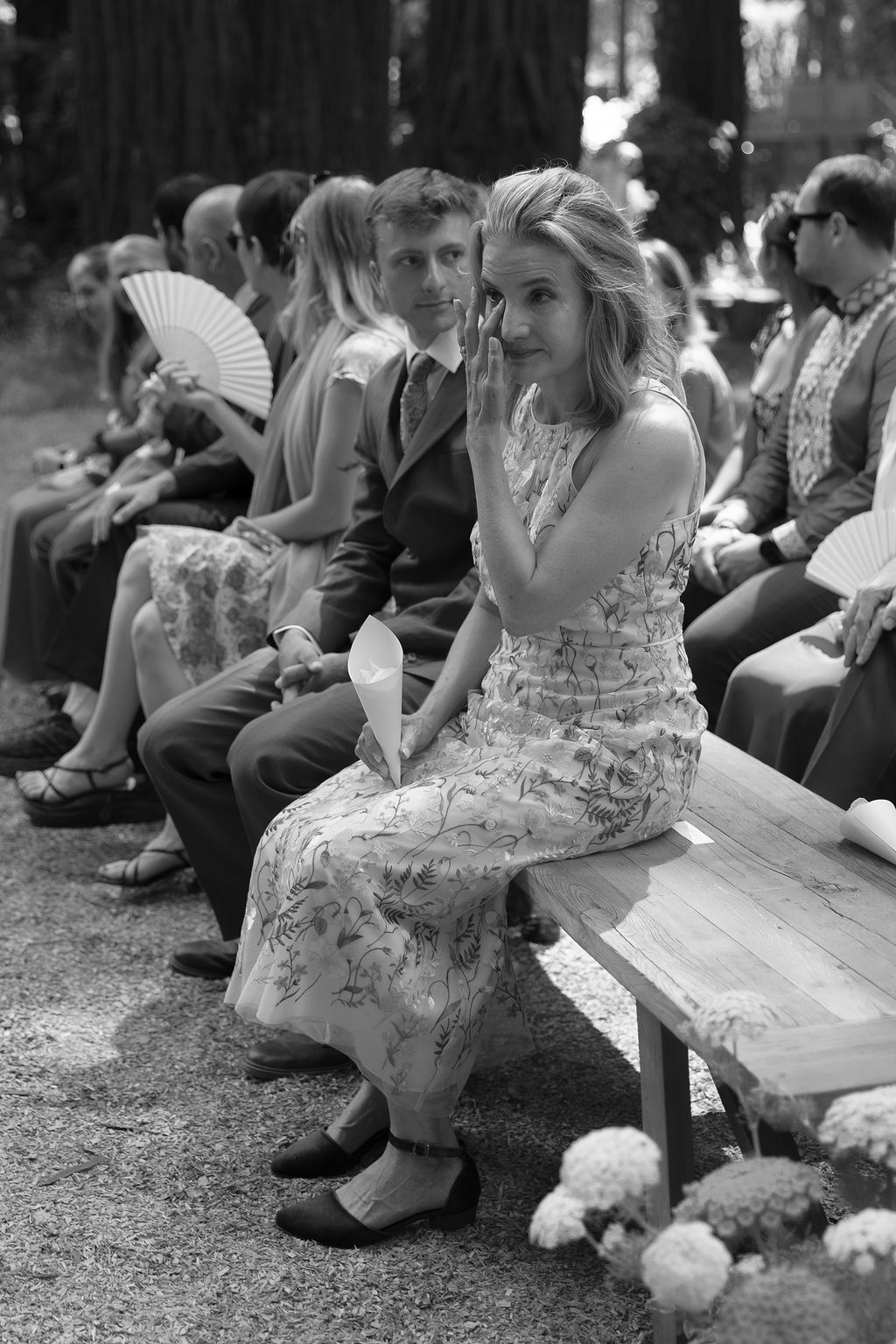 Wedding guests seated on ground during outdoor forest ceremony.