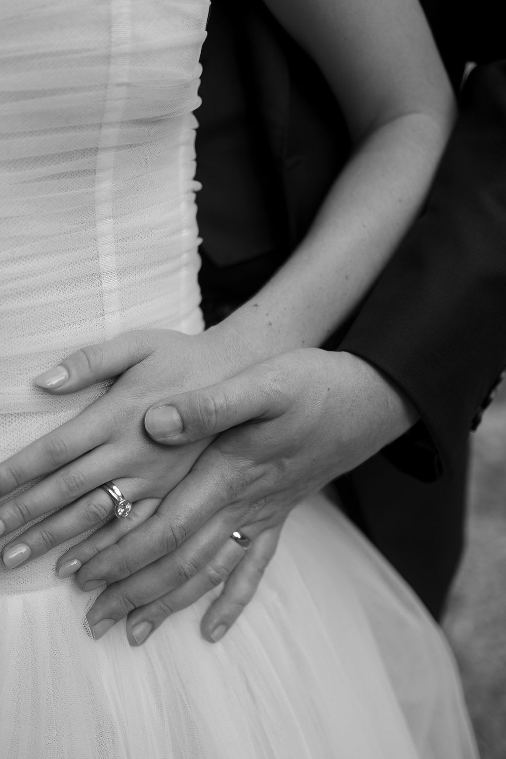Close-up black and white shot of hands with wedding ring resting on white tulle fabric.