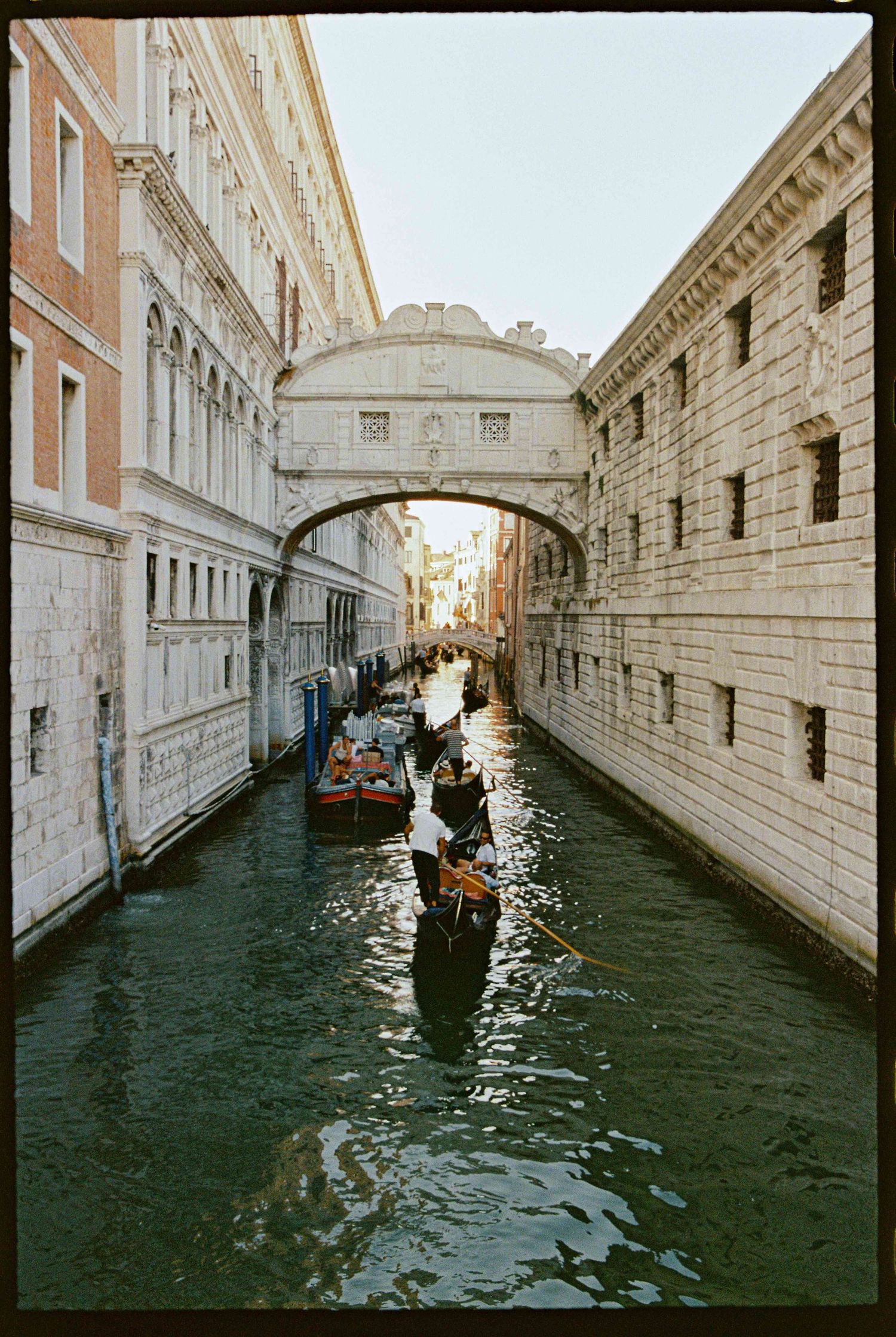 Gondolas gliding through Venice canal under the iconic Bridge of Sighs, flanked by historic stone buildings.