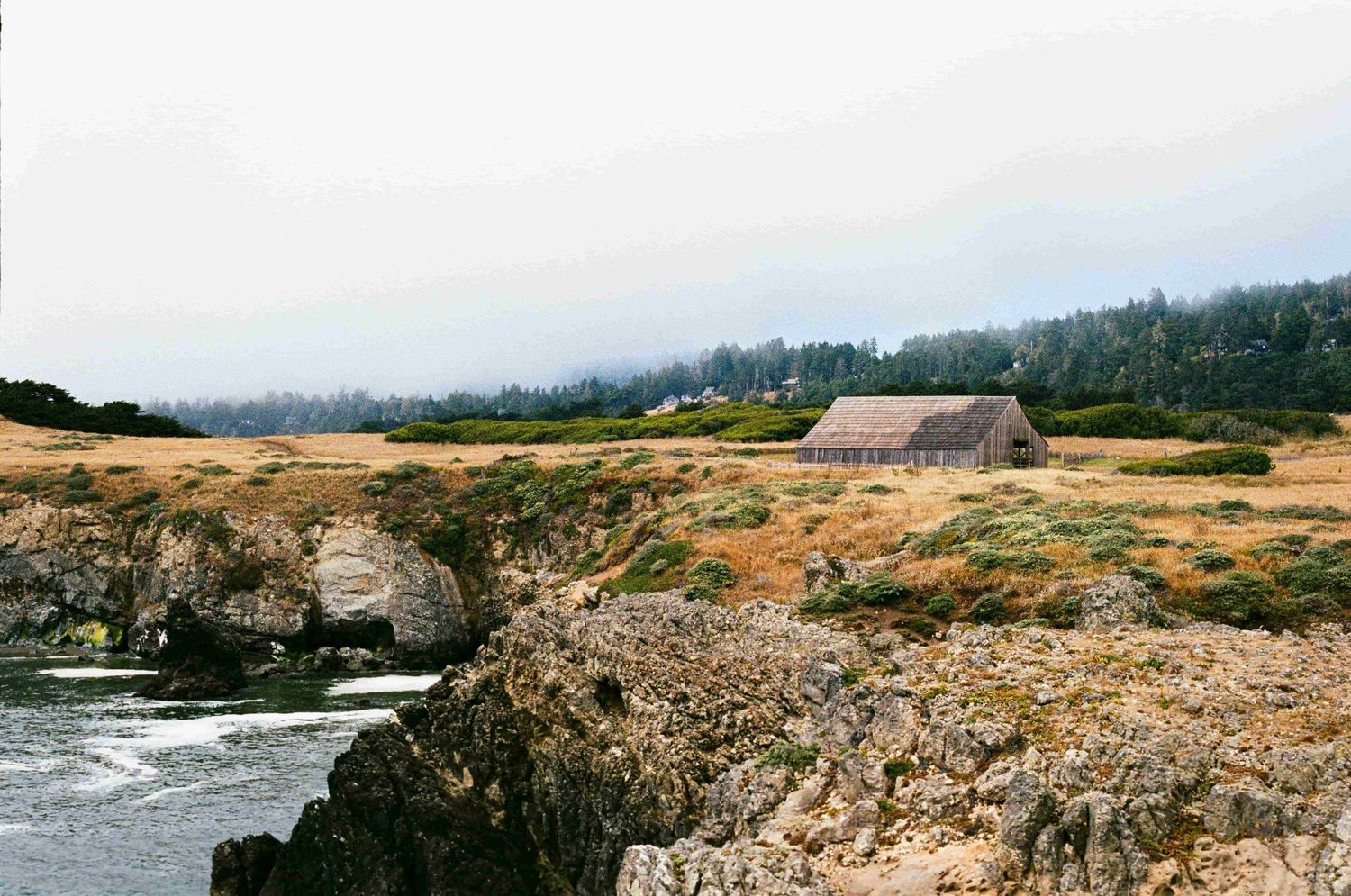 Panoramic view of the rugged Oregon coastline shows waves crashing against rocky cliffs and windswept beaches.