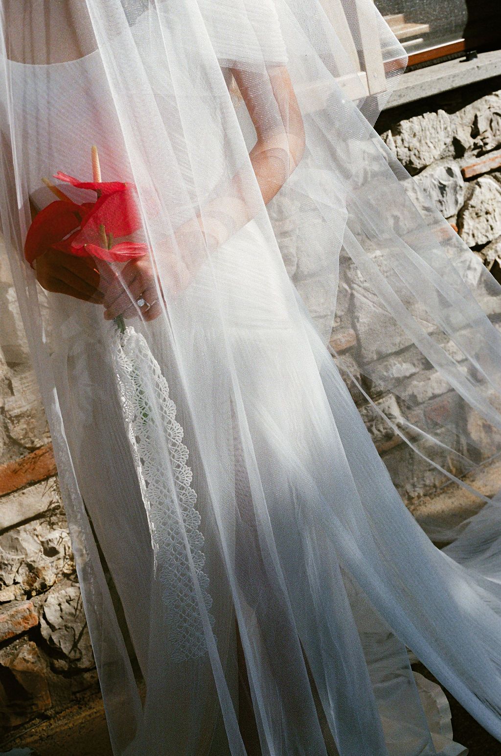 Delicate lace and tulle details of a flowing white dress captured against weathered stone walls in Tuscany, Italy.