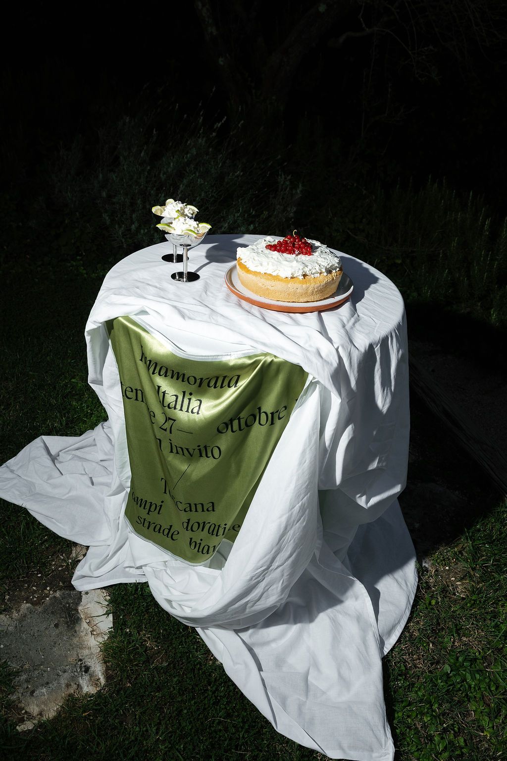 White tablecloth covered picnic setting with dessert plates and vintage decorative elements in Tuscany, Italy.