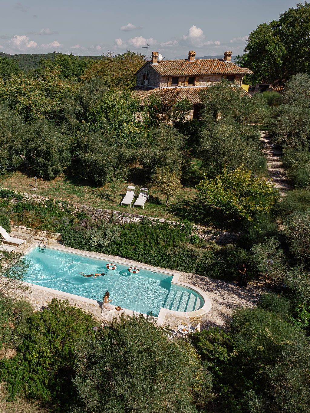 Scenic swimming pool nestled in the Italian countryside with stone buildings and mountains in the background in Tuscany, Italy.