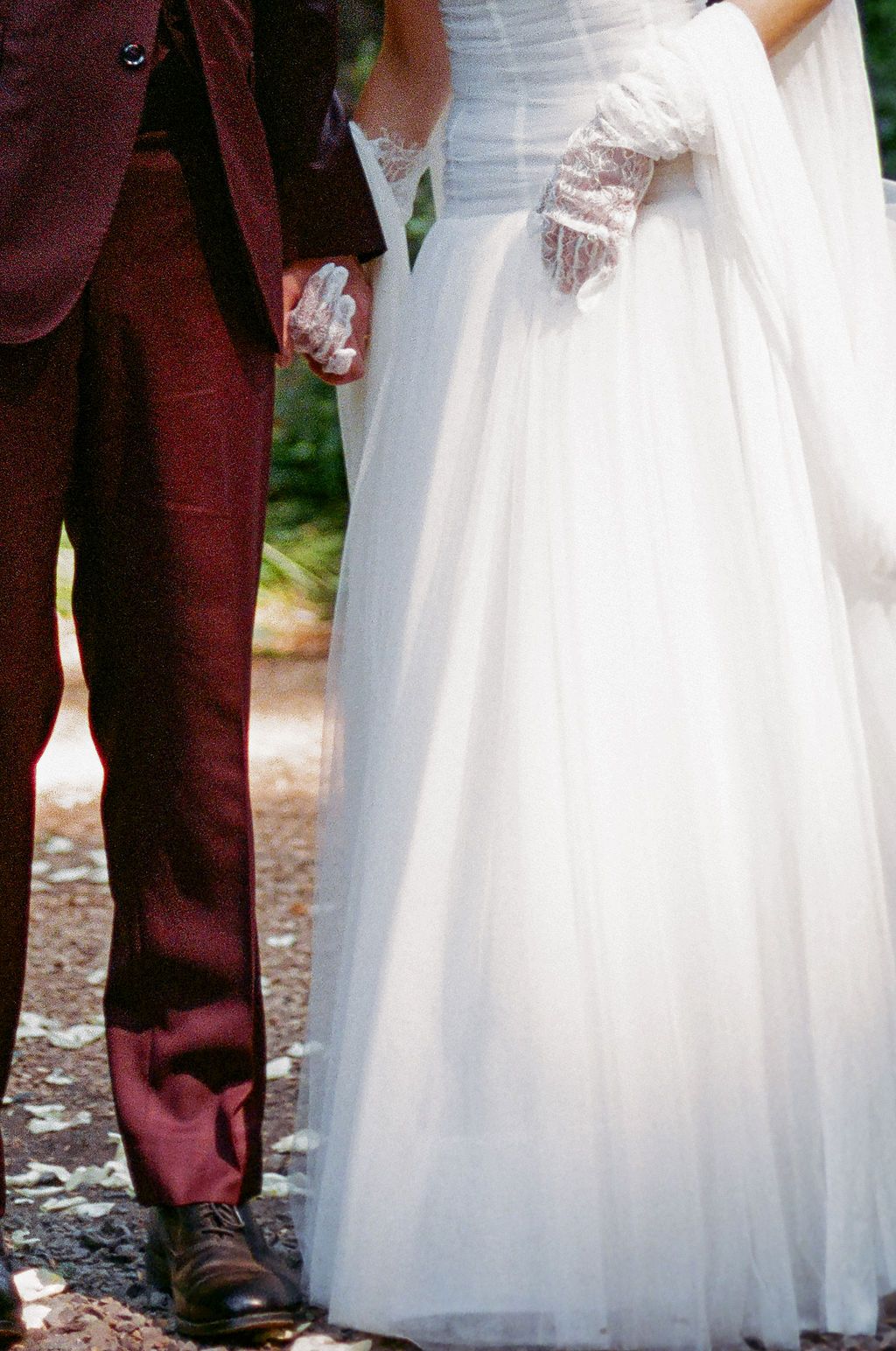 Close-up details of a white wedding dress against burgundy attire in a forest setting.