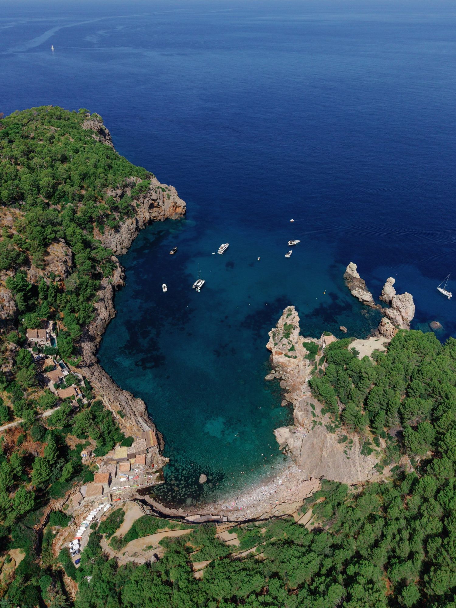 Aerial view of a secluded turquoise cove surrounded by lush green cliffs and rocky formations in the Mediterranean Sea.